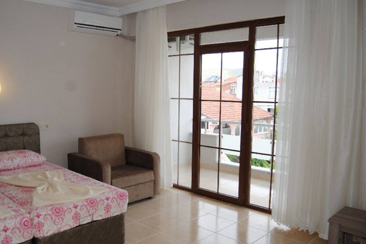 A hotel room with a bed, a chair, a sliding glass door to the balcony, and a wall-mounted air conditioner.