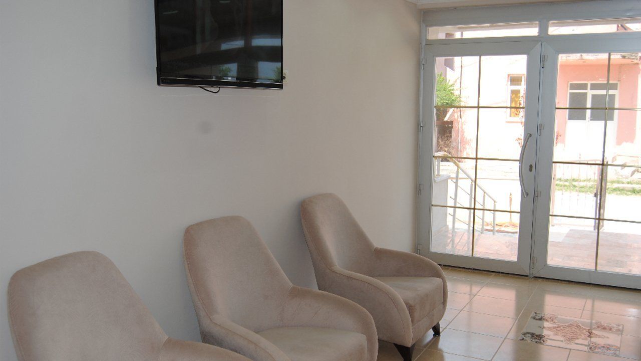 A room with two beige armchairs, a flat-screen TV mounted on the wall, and a sliding glass door leading to an outdoor area.