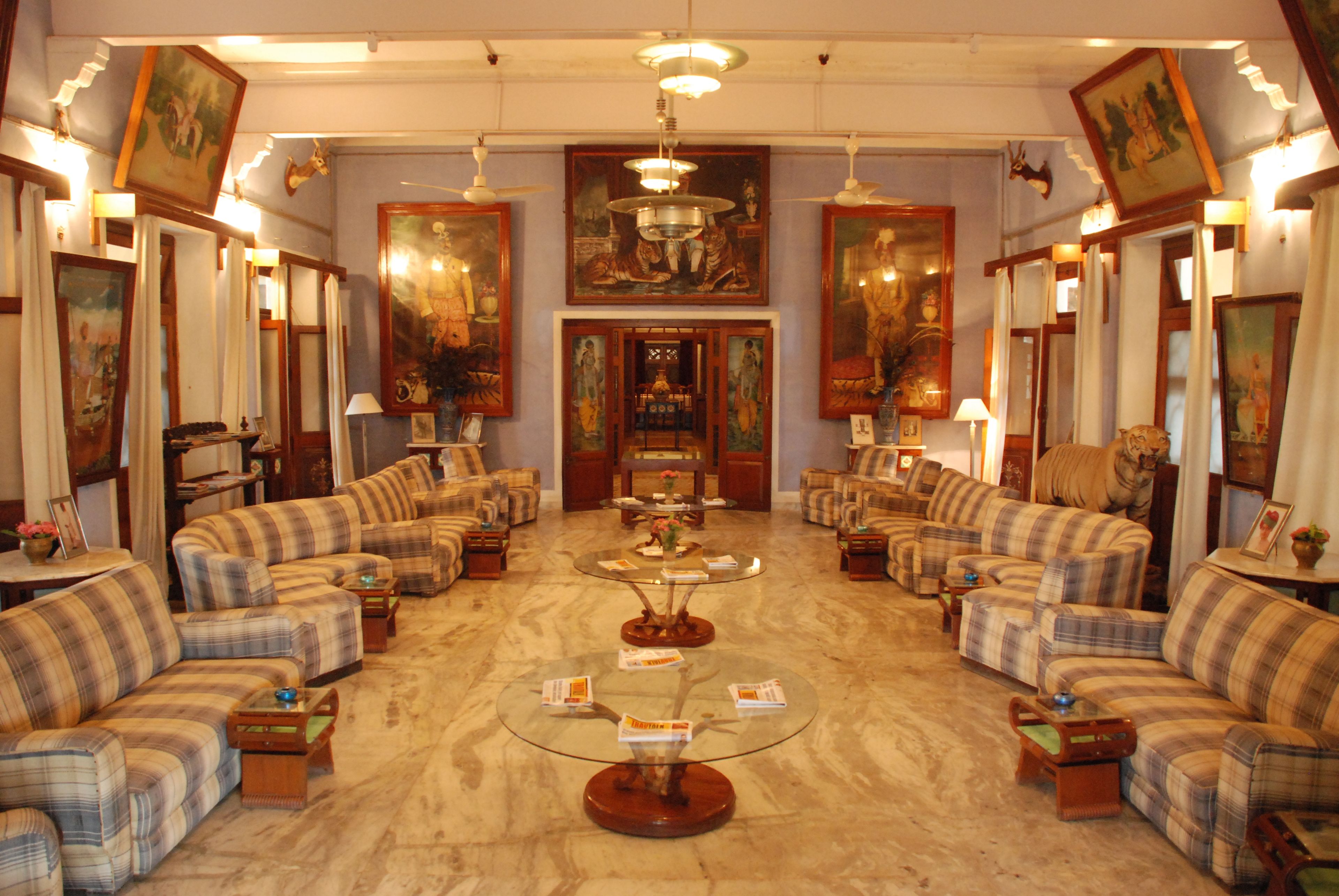 Um saguão de hotel com uma mesa de centro cercada por sofás e poltronas, obras de arte nas paredes e um lustre.