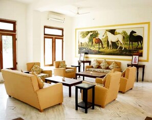 A spacious living room with a large painting of horses, multiple sofas, and a coffee table. - Bhanwar Vilas Palace (Karauli)
