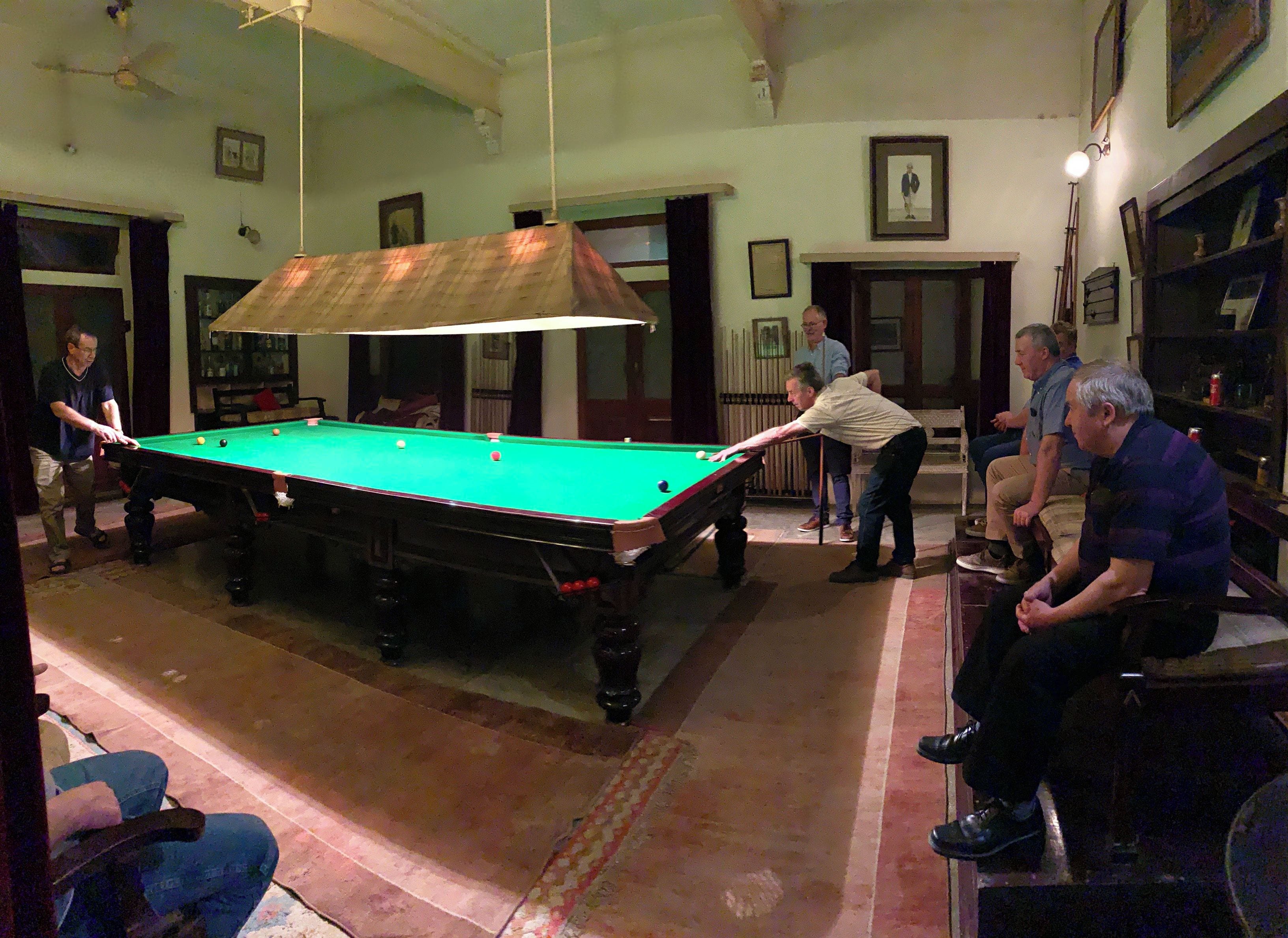 A pool table in a room with a ceiling fan, framed pictures on the walls, and a patterned carpet.