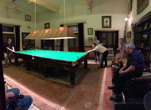 A pool table in a room with a ceiling fan, framed pictures on the walls, and a patterned carpet. - Bhanwar Vilas Palace (Karauli)