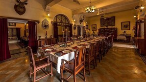 A formal dining room with long tables set for a meal, wooden chairs, and a chandelier. - Bhanwar Vilas Palace (Karauli)
