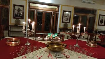 A dining area with tables set for a meal, featuring candles, glassware, and a central brass bowl.