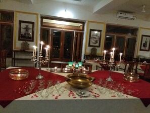 A dining area with tables set for a meal, featuring candles, glassware, and a central brass bowl. - Bhanwar Vilas Palace (Karauli)