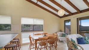 A spacious room with a wooden dining table and chairs, a wicker sofa, and a large window offering a view of the outdoors. - Galleries 3 - 3/28 Peregian Esplanade (Peregian Beach)