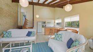 A spacious living area with a kitchen in the background, featuring a wooden ceiling and large windows. - Galleries 3 - 3/28 Peregian Esplanade (Peregian Beach)
