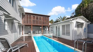 A swimming pool with a wooden deck, a covered seating area, and a two-story building with a balcony. - Sea Splash 75 Lorikeet Drive (Peregian Beach)