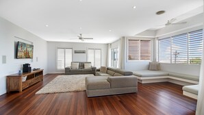 A spacious living room with a wooden floor, a grey sectional sofa, a wooden cabinet, and a painting on the wall. - Sea Splash 75 Lorikeet Drive (Peregian Beach)