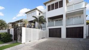 A modern two-story house with a garage, a covered patio area, and a stone wall. - Sea Splash 75 Lorikeet Drive (Peregian Beach)