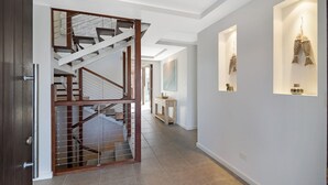 A modern interior with a staircase, a hallway, and wall-mounted display cases. - Sea Splash 75 Lorikeet Drive (Peregian Beach)