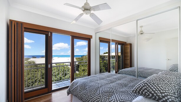 A bedroom with a bed, a ceiling fan, and a large window with a view of the beach. - Notre Reve - 2/4 Brolga Place (Peregian Beach)