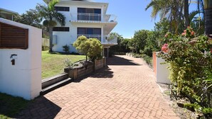A two-story house with a balcony, a paved driveway, and surrounding greenery. - Notre Reve - 2/4 Brolga Place (Peregian Beach)