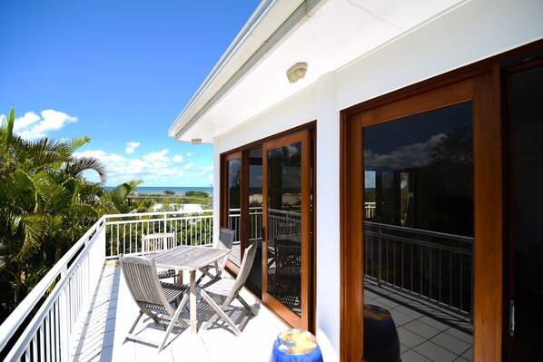 A balcony with a table and chairs, a view of the ocean, and a wooden door.
