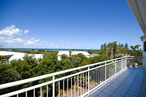 A balcony with a white railing overlooking a view of the ocean and a residential area.