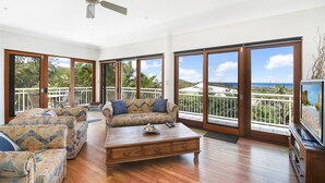 A spacious living room with a wooden coffee table, patterned sofas, and large sliding glass doors offering a view of the ocean. - Notre Reve - 2/4 Brolga Place (Peregian Beach)