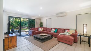 A modern living room with a sectional sofa, a coffee table, and a TV on a wooden cabinet. - Home Away From Home, 38 Redwood Avenue, Marcus Beach, Noosa Area (Marcus Beach)