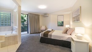 A hotel room with a bed, a nightstand, a bedside lamp, a window, a bathroom with a bathtub, and a sliding door leading to a balcony. - Home Away From Home, 38 Redwood Avenue, Marcus Beach, Noosa Area (Marcus Beach)