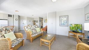A spacious living room with wicker furniture, a glass coffee table, and a television.