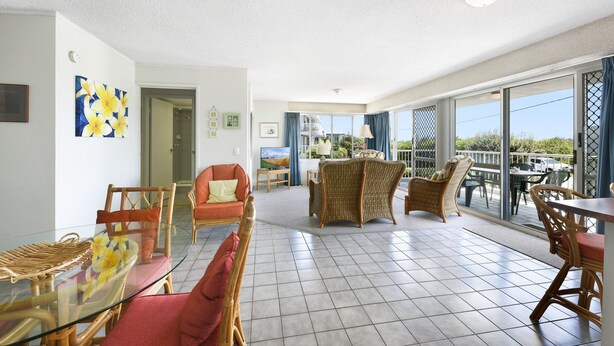 A spacious living area with a glass dining table, wicker chairs, and a balcony with outdoor seating.