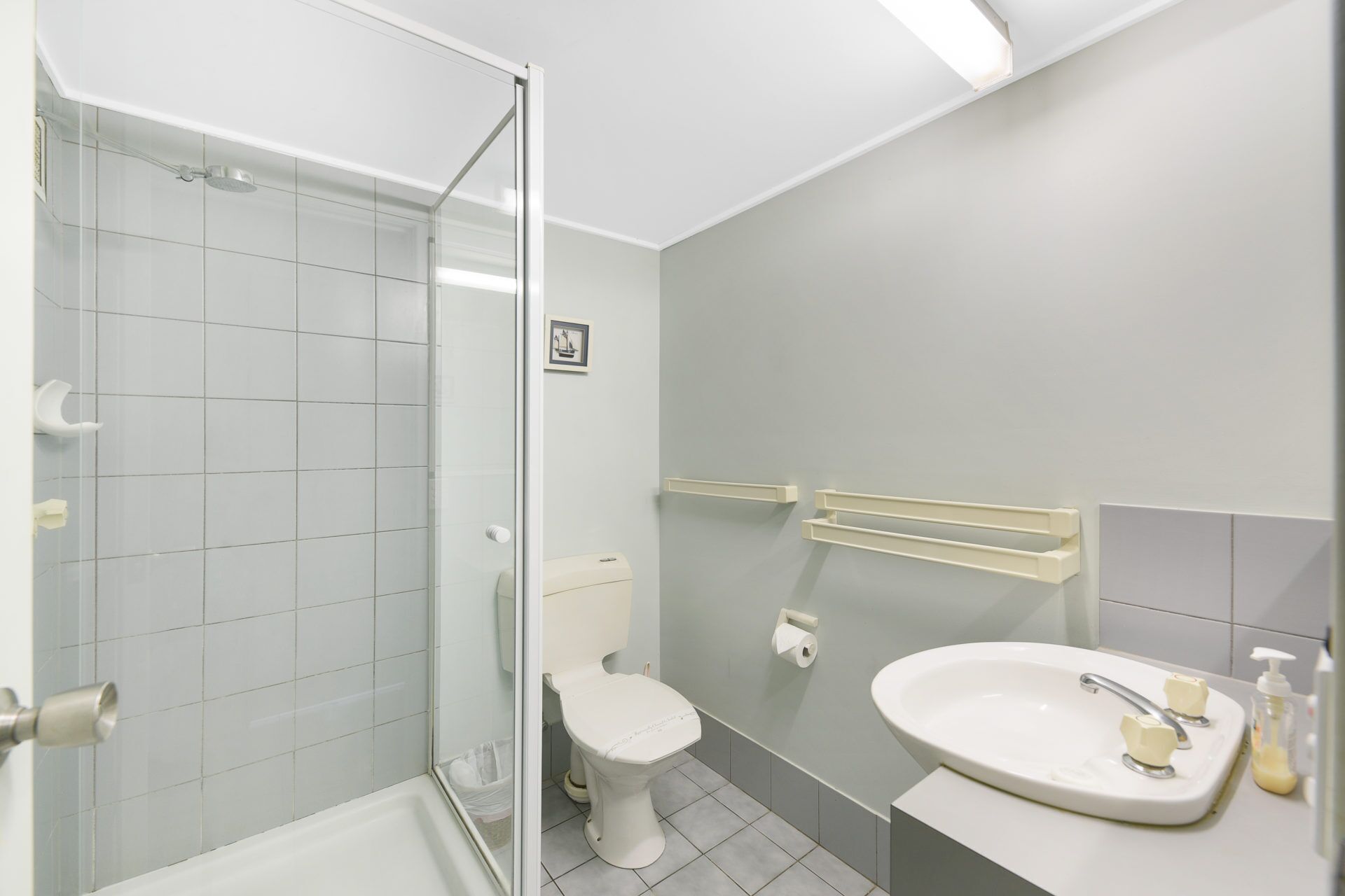 Un baño moderno con cabina de ducha de vidrio, inodoro, lavabo con dispensadores de jabón y perchero para toallas.