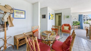 A spacious living area with wicker furniture, a glass coffee table, and a view of a balcony.