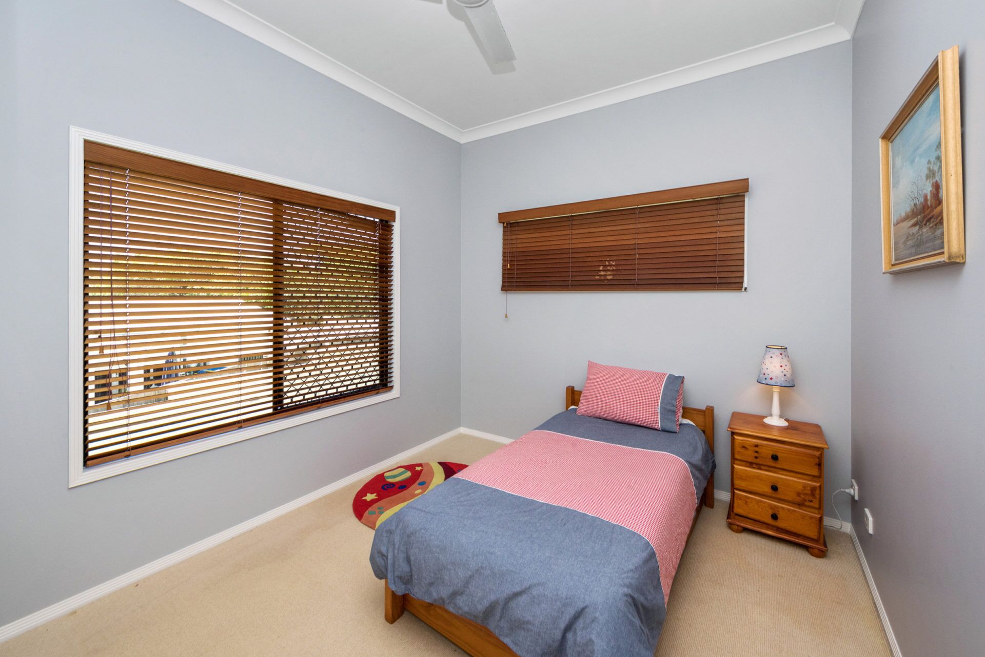 A bedroom with a bed, a nightstand, a lamp, and two windows with blinds.