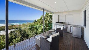 A balcony with a view of the ocean, a grill, and wicker furniture.