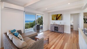 A spacious living room with a large sliding glass door leading to a balcony, a wooden floor, a sofa with patterned cushions, and a wooden cabinet.