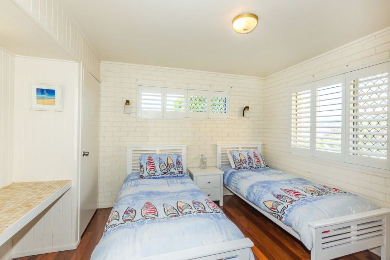 A bedroom with two beds, white walls, and a small desk.