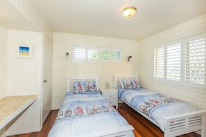 A bedroom with two beds, white walls, and a small desk.