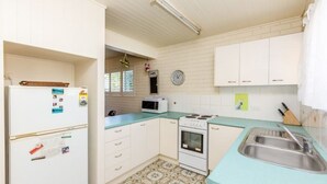 A compact kitchen with white cabinets, a microwave, an oven, and a sink. - Lyrona - 3/35 Avocet Parade (Peregian Beach)