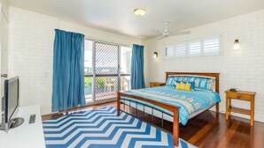 A bedroom with a bed, a desk, a TV, and a balcony with blue curtains. - Lyrona - 3/35 Avocet Parade (Peregian Beach)