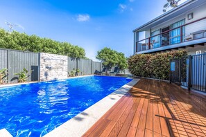 A swimming pool with a wooden deck, a stone wall, and a fenced area with greenery. - Lyrona - 3/35 Avocet Parade (Peregian Beach)