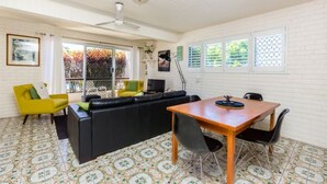 A spacious living area with a black sofa, yellow armchair, and a wooden dining table with chairs. - Lyrona - 3/35 Avocet Parade (Peregian Beach)