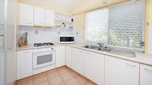 A kitchen with white cabinets, a gas stove, a microwave, and a window with blinds.