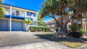 A residential building with a garage, a small garden, and a palm tree.