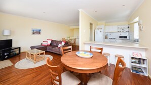 A compact living space with a dining area, a sofa, a TV, and a kitchen in the background.