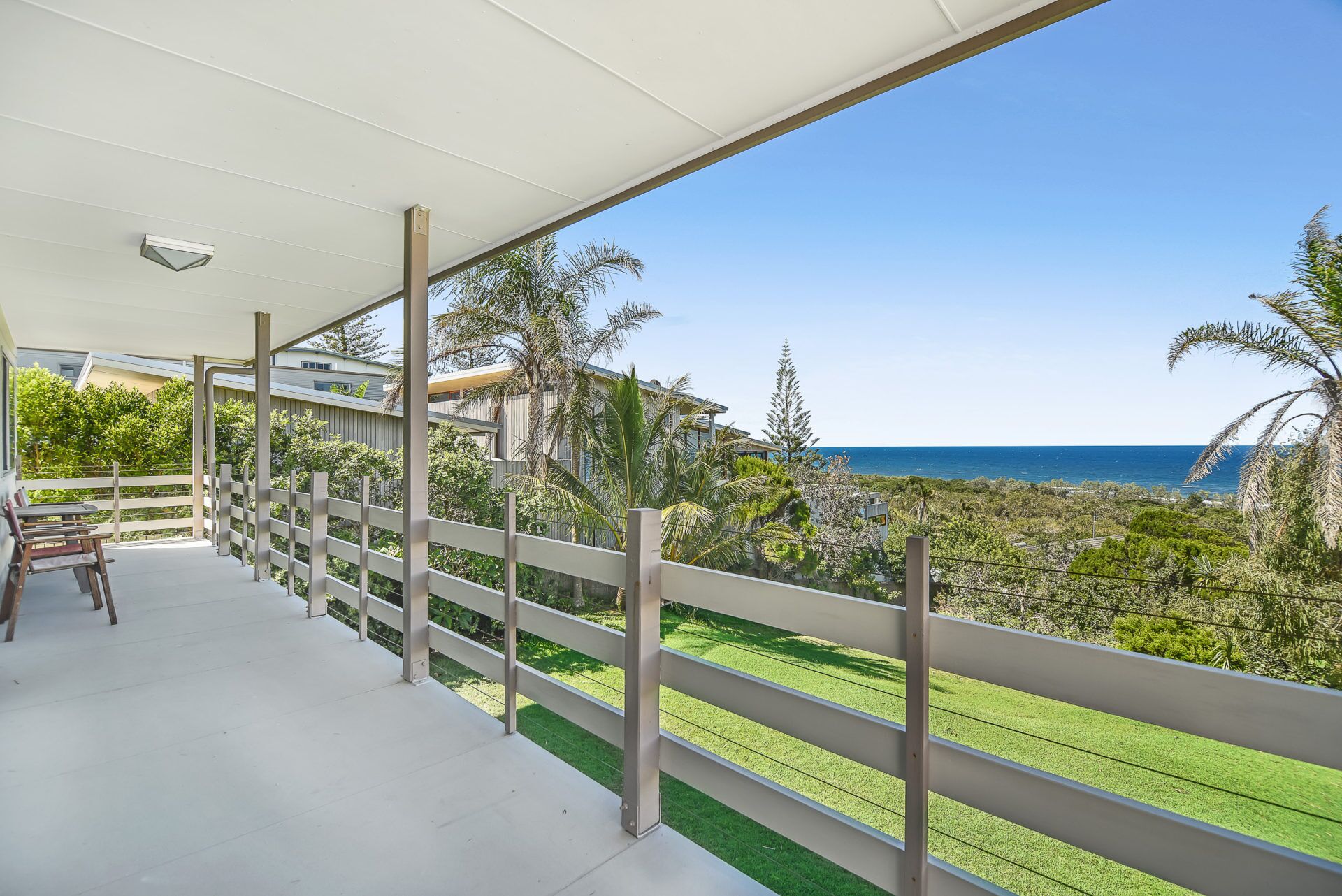 A covered balcony with a view of the ocean, a wooden fence, and a table with chairs.