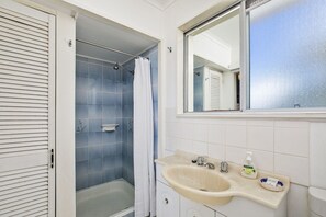 A bathroom with a shower, a sink with a mirror, and toiletries. - Sea Shack - 29 Pelican Street, Peregian Beach, Noosa Area (Peregian Beach)