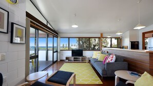 Una sala de estar moderna con sofá, sillas, televisor y una cocina con vistas al exterior.