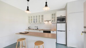 Eine moderne Küche mit weißen Schränken, einer Mikrowelle, einem Kühlschrank und zwei Holzhockern.