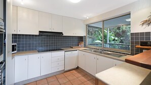 A modern kitchen with white cabinets, a black tiled backsplash, a window with a view of greenery, and a built-in microwave.