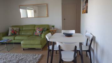 A living room with a green sofa, white chairs, a small table with a bowl, a fluffy rug, and a mirror on the wall.