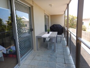 Un balcon avec une table et des chaises, un barbecue et une porte-fenêtre coulissante.