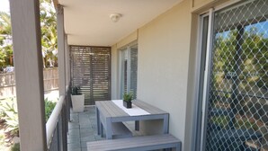 A balcony with two wooden tables and a bench, a potted plant, and a sliding glass door with a mesh screen. - Unit 2 at 4 Pelican Street, Peregian Beach, Noosa Area (Peregian Beach)