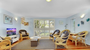 A spacious living room with wicker furniture, a flat-screen TV, and large windows with blinds. - Allamanda Sands - 23 Oriole Avenue (Peregian Beach)