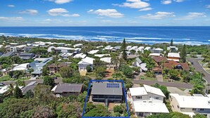 An aerial view of a coastal residential area with houses, a clear blue sky, and the ocean in the background. - Allamanda Sands - 23 Oriole Avenue (Peregian Beach)