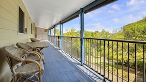 A covered porch with wicker chairs and a table, overlooking a garden with trees and shrubs. - Allamanda Sands - 23 Oriole Avenue (Peregian Beach)