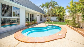 A backyard with a swimming pool, a house with large windows, and a fenced yard with palm trees. - Allamanda Sands - 23 Oriole Avenue (Peregian Beach)